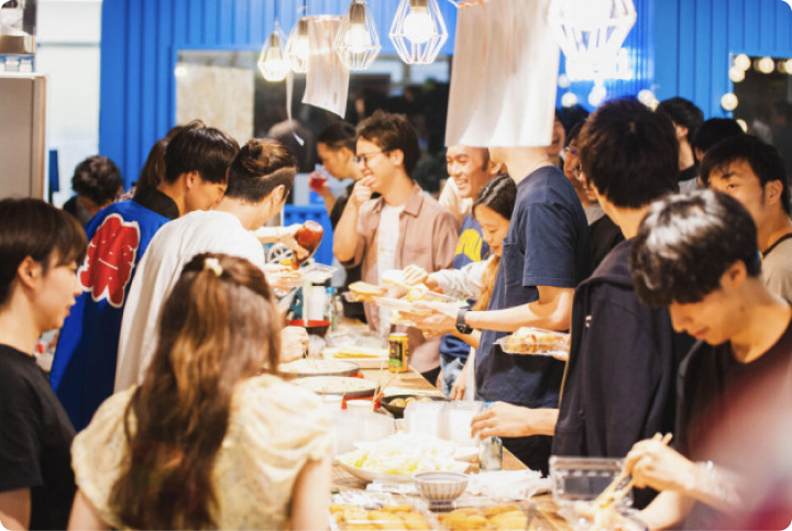 社内イベントで多くのメンバーが並んで料理を取り分けながら交流している様子。