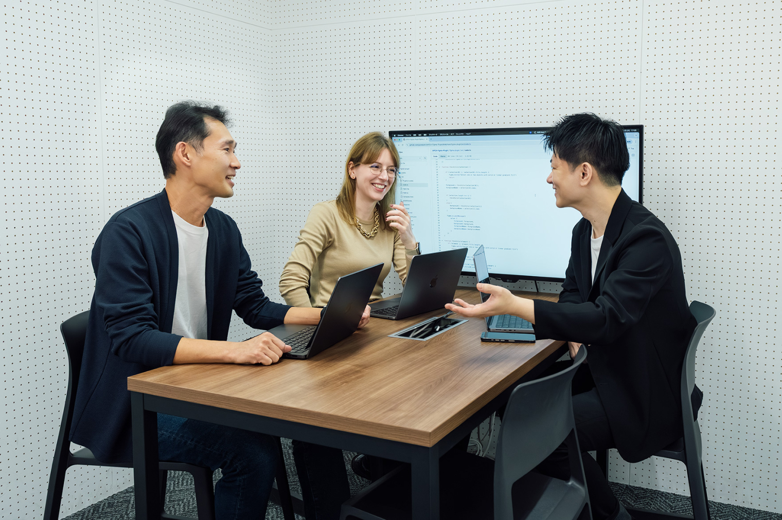 会議室のテーブルで、ノートPCを前に3人が打ち合わせをしている様子。