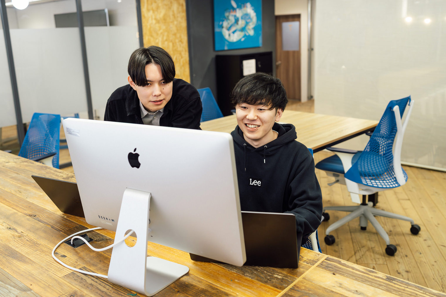 2名の社員が外付けモニターを前に、コミュニケーションをとりながら作業している様子。