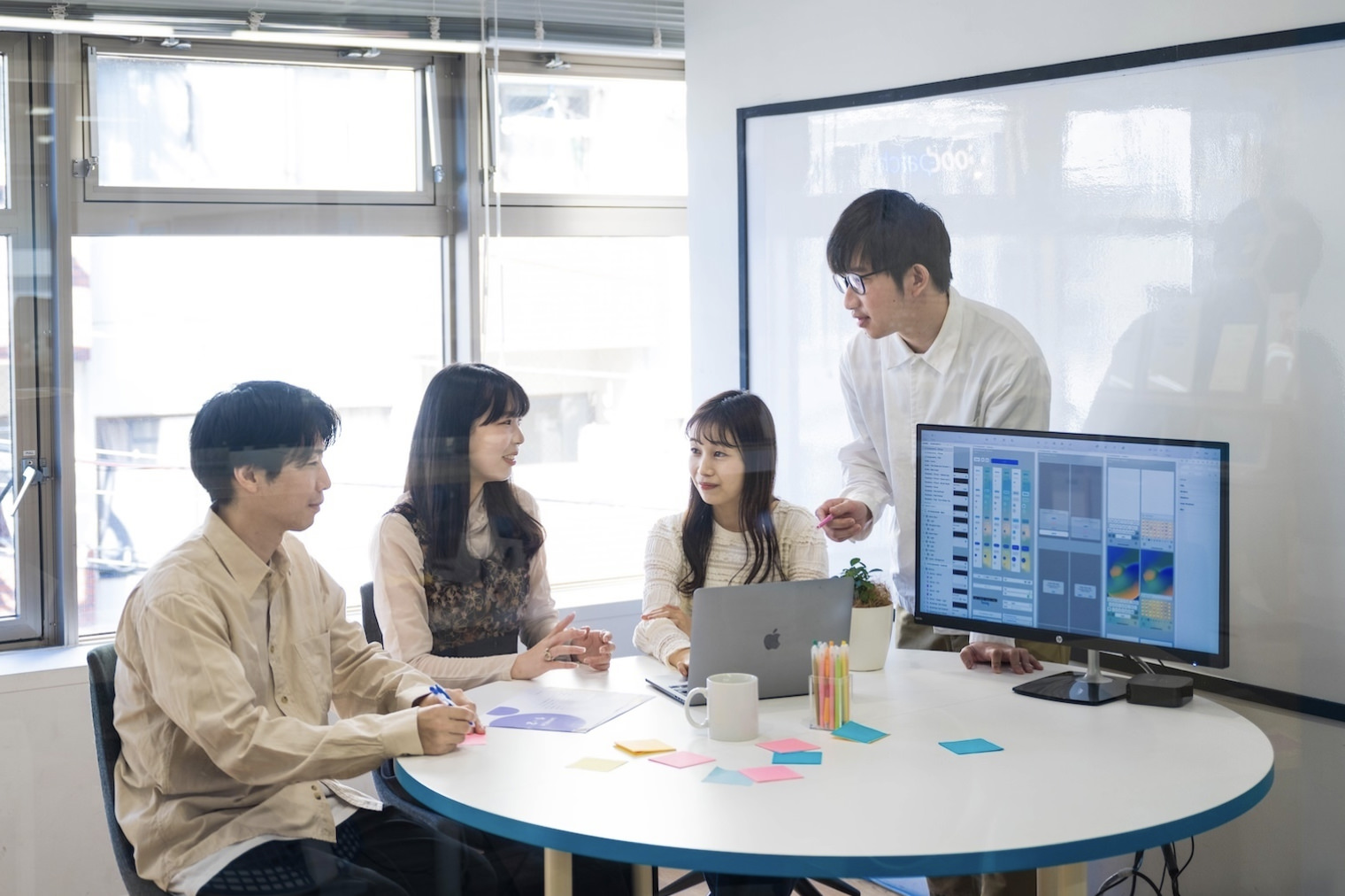 円卓を囲み、モニターに資料を映しながら、4名の社員が打ち合わせしている様子。