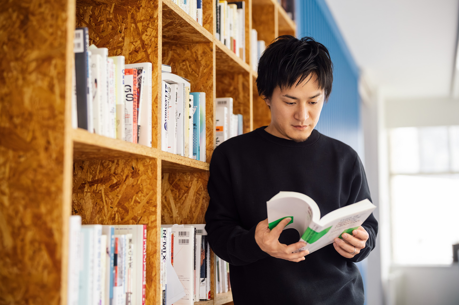 本棚の前に立ち、書籍を手に取って読んでいる社員の様子。