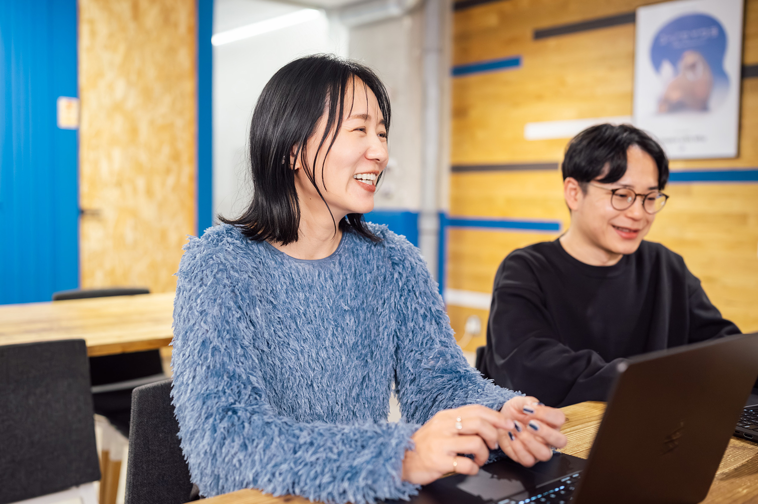 オフィスで女性と男性の社員がノートパソコンを使いながら会話している様子。