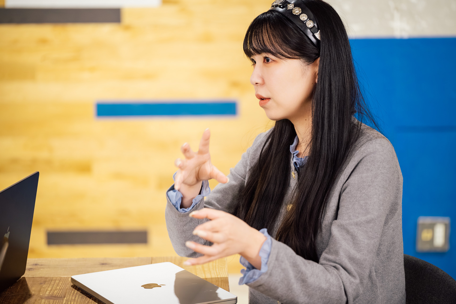 オフィスで女性の社員がノートパソコンの前で、身振りを交えながら話している様子。