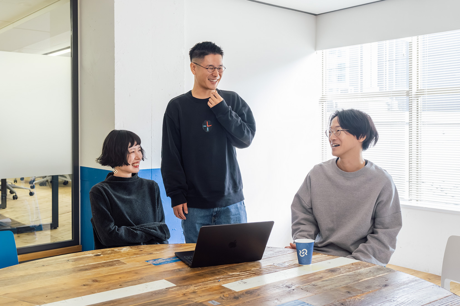 円卓を3名の社員が囲い、会話をしながら笑顔でコミュニケーションを取る社員の様子。